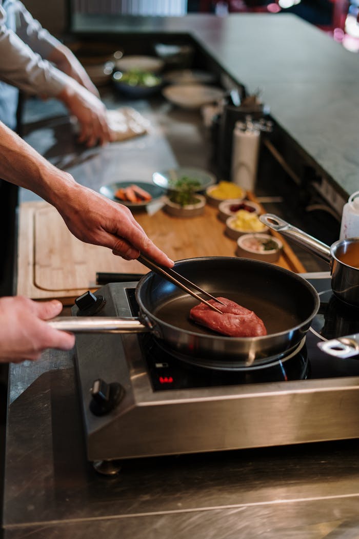 Chef expertly cooks steak in an open kitchen with modern cookware, highlighting culinary skills.
