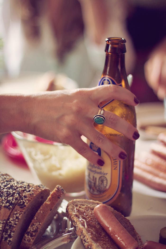 about-me-img A hand holding a beer bottle at a German-style dinner with bread and sausages.