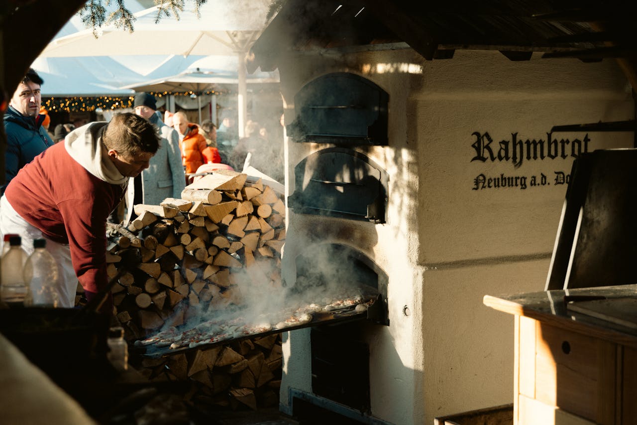 Street vendor baking traditional bread at Berlin Christmas market with wood-fired oven.
